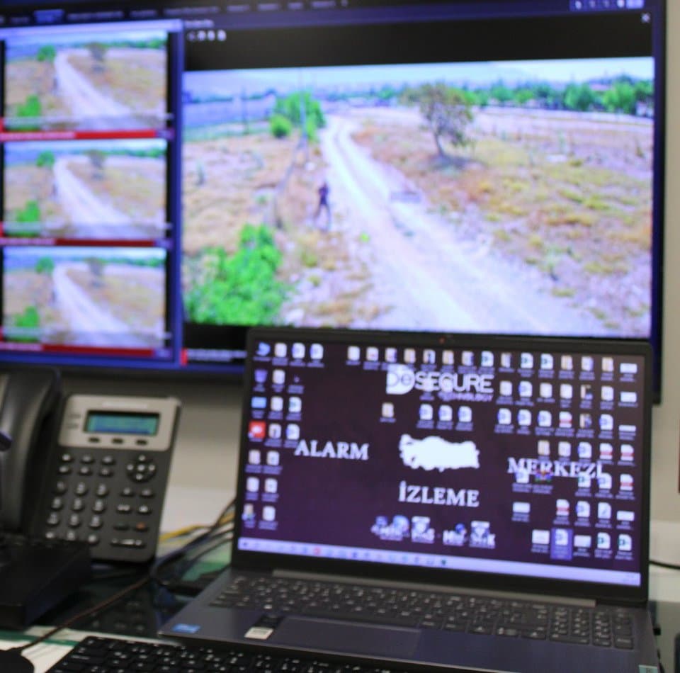 Alarm İzleme Merkezi'nde operatör konsolu: bir ana kamera görüntüsü, yanında üç küçük görüntü, telefon ve dizüstü bilgisayar