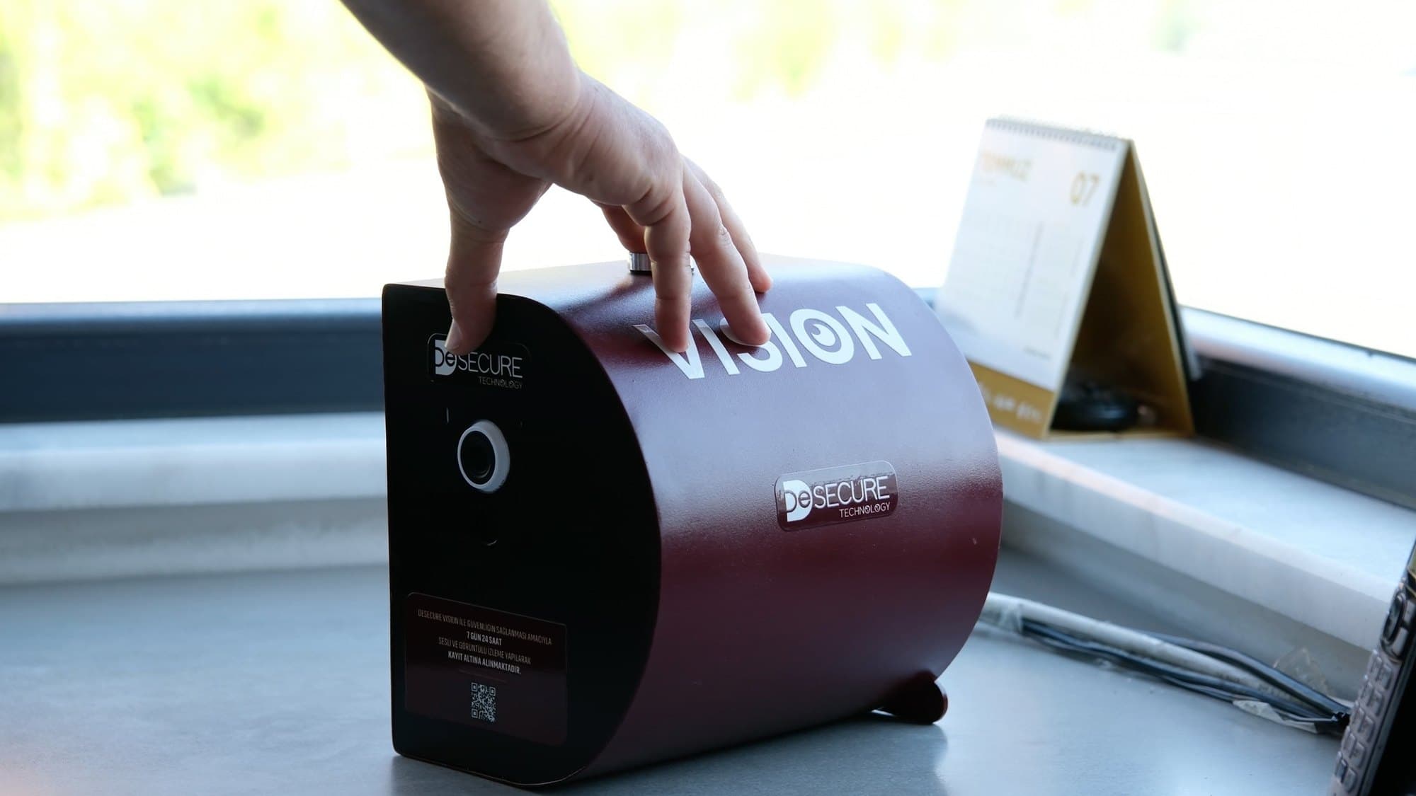 Elle tutulan bordo gövdeli Desecure Vision cihazı; ön yüzünde kamera merceği, üstünde VISION yazısı